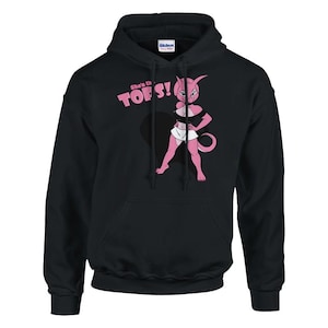 Puede incluir: Una sudadera negra con capucha que presenta un gráfico de un personaje antropomórfico rosa con un top negro y una falda blanca. El texto "She's the TOPS!" está impreso en rosa sobre el personaje. La sudadera tiene mangas largas y un bolsillo.