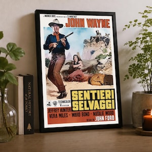 Peut inclure: Une affiche de film encadrée pour Sentieri Selvaggi avec John Wayne. L'illustration montre un homme au chapeau de cow-boy tenant un fusil, une femme en robe marron et une silhouette allongée au sol. Le texte inclut le titre et les acteurs.