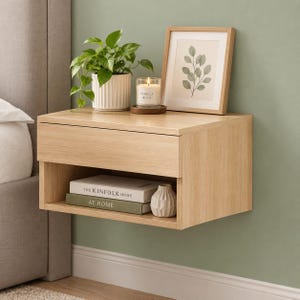 May include: A light oak floating nightstand with one drawer and an open shelf. On top sits a green plant in a white ribbed pot, a vanilla bean candle, and a framed botanical print. Inside the shelf are two books and a small white vase.