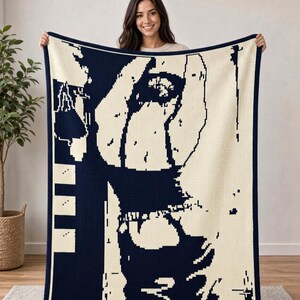 May include: A rectangular knit throw blanket featuring a high-contrast, two-tone graphic design in navy blue and cream. The pattern displays a stylized, pixelated silhouette of a person with arms raised, framed by a solid navy blue border.