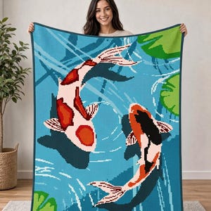 May include: A rectangular crochet blanket featuring a pixelated design of two koi fish swimming in blue water with green lily pads. The fish are white with orange and black markings, depicted in a circular motion against a textured blue background.