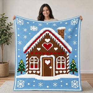 May include: A rectangular crochet blanket featuring a brown gingerbread house design on a light blue background with white snowflakes. The house has a red roof, a chimney, two windows, a door with a heart, and two green Christmas trees.