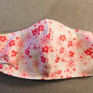 May include: A pink and white face mask with a floral pattern. The mask has a pink elastic band.