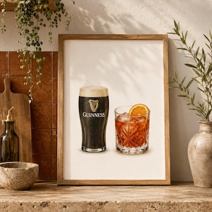 Puede incluir: Una lámina enmarcada que muestra una cerveza negra Guinness en un vaso de pinta con espuma cremosa y el logotipo de un arpa dorada, junto a un vaso de cristal con un cóctel de color ámbar, cubitos de hielo y una rodaja de naranja fresca.