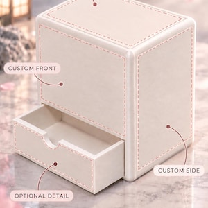 Könnte beinhalten: Eine cremefarbene Aufbewahrungsbox mit einer ausziehbaren Schublade. Die Box enthält Beschriftungen für anpassbare Bereiche: YOUR DESIGN HERE auf der Oberseite, CUSTOM FRONT auf der Vorderseite, CUSTOM SIDE an der Seite und OPTIONAL DETAIL an der Schublade.