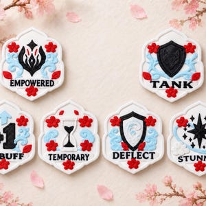 Pode incluir: Seis fichas hexagonais brancas com detalhes de flores de cerejeira vermelhas e padrões de redemoinho azul-claro. Cada ficha exibe um ícone preto e texto único: EMPOWERED, TANK, +1 BUFF, TEMPORARY, DEFLECT e STUNNED, representando efeitos de jogo.