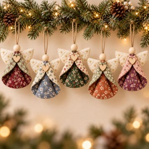 Könnte beinhalten: Fünf Stoffengel-Ornamente hängen an einem Tannenzweig. Jeder Engel hat gesteppte cremefarbene Flügel, einen Holzkopf, ein kleines Herz aus Holz und ein Kleid mit Blumenmuster in Rot, Blau, Dunkelgrün, Orange oder Violett.