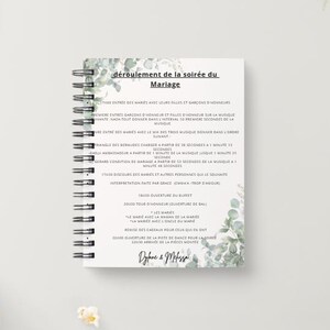 Op de afbeelding: Een spiraalgebonden trouwprogramma-notitieboek met een witte kaft en illustraties van groene eucalyptusbladeren. De tekst luidt "déroulement de la soirée du Mariage", gevolgd door een gedetailleerd schema en de namen "Dylane & Melissa" onderaan.
