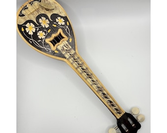 Peut inclure: Un instrument à cordes en forme de poire avec un corps en bois clair, des accents peints en noir et des motifs floraux jaunes. Le manche présente une touche détaillée avec des motifs décoratifs et quatre chevilles blanches.