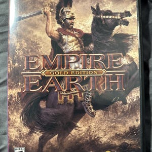 May include: A PC DVD-ROM game case for Empire Earth Gold Edition. The cover art features a warrior in a helmet and armor riding a dark horse while holding a sword aloft. The title text is centered, and the ESRB Teen rating and Sierra logo are visible.
