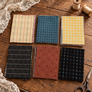 May include: Six rectangular fabric swatches featuring various patterns including vertical stripes, small grids, and dots in colors of cream, blue, yellow, dark gray, rust orange, and black, arranged in two rows of three on a wooden surface.