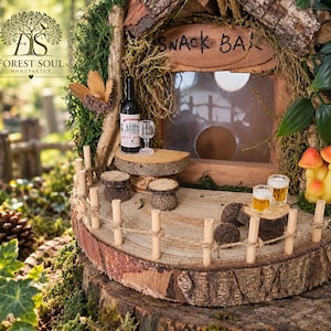 Może przedstawiać: Miniaturowy drewniany bar z dachem pokrytym korą, małym stolikiem z butelką wina i kieliszkiem, dwoma stołkami oraz ogrodzonym patio. Scena zawiera dwa małe kufle piwa i dekoracyjne pomarańczowe grzyby.