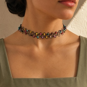 May include: A black plastic tattoo-style choker necklace featuring a repeating looped wire pattern. The design is accented with small, round, multi-colored beads in shades of pink, yellow, blue, and purple, evenly spaced throughout the structure.