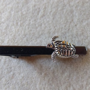 May include: A silver turtle tie clip with a black metal bar.