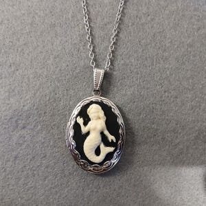 Puede incluir: Un collar de cadena de plata con un medallón de camafeo blanco y negro con un diseño de sirena.