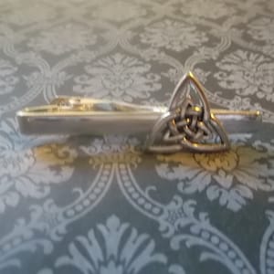 May include: Silver tie clip featuring a Celtic knot design. The knot is a traditional symbol of love, friendship, and unity.