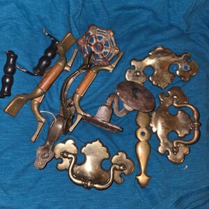 May include: A collection of assorted metal hardware including brass drawer pulls with ornate backplates, two metal handles with wooden grips, a circular rusted metal valve wheel, and a single rusted metal hook with a round mounting plate.