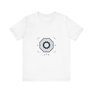 May include: A white short-sleeve t-shirt featuring a centered dark navy blue graphic. The design consists of a multi-layered octagon surrounding a star-like shape, accented by small geometric symbols and zigzag lines positioned around the perimeter.