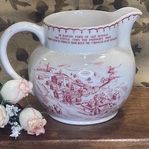 May include: A cream-colored ceramic pitcher featuring a red transferware print of a historic Boston town map. The text reads: In Boston town of old renown, the gentle cows the pathways made, some crew to streets that keep the stranger quite dismayed.