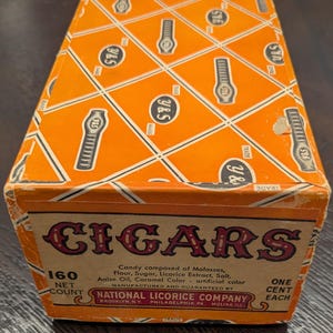 May include: A rectangular orange box with a white diamond grid pattern featuring Y&S logos. The front panel reads CIGARS, 160 NET COUNT, ONE CENT EACH, and lists ingredients including molasses, flour, sugar, and licorice extract by National Licorice Company.