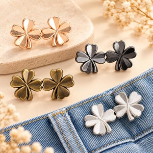 May include: Four pairs of clover-shaped metal buttons in rose gold, black, antique bronze, and silver tones. Each button features a four-leaf clover design with a smooth, polished finish on the petals and a central stem detail for garment fastening.