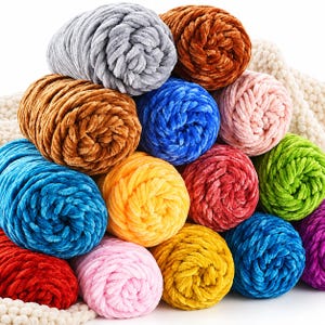 May include: A collection of thick, plush chenille yarn skeins in a variety of vibrant colours including grey, brown, blue, pink, yellow, red, green, and purple, arranged in a stacked pile with a textured cream-coloured fabric base underneath.