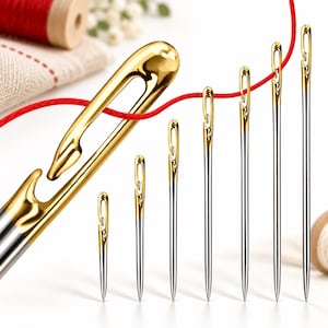 May include: A set of seven sewing needles arranged in a row, featuring silver-toned shafts and polished gold-toned eyes with an open-ended design. A single red thread is threaded through the eyes of the needles, connecting them in a horizontal line.