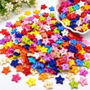Könnte beinhalten: Eine große Ansammlung kleiner, sternförmiger Knöpfe in verschiedenen leuchtenden Farben wie Rot, Blau, Gelb, Grün, Pink und Weiß. Jeder Knopf hat zwei Löcher in der Mitte. Einige Knöpfe liegen lose verstreut, andere befinden sich in einer weißen Schale.