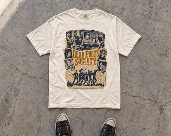 Könnte beinhalten: Ein cremefarbenes Kurzarm-T-Shirt mit einem Grafikdruck, der den Text Dead Poets Society und O Captain My Captain enthält. Das Design umfasst schwarz-weiße Filmszenen, Silhouetten von Personen und handschriftliche Notizen auf beigem Grund.