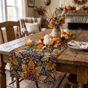 May include: A rectangular table runner featuring a dark blue background with a repeating pattern of golden yellow autumn leaves and small red berries. The runner is placed on a wooden table with a centerpiece of white and orange pumpkins.