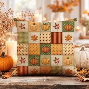 May include: A square throw pillow featuring a patchwork design of alternating squares. The pattern includes illustrations of orange pumpkins, brown autumn leaves, and various geometric textures in shades of green, yellow, and orange.