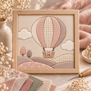 Könnte beinhalten: Ein quadratisches, gerahmtes Wandbild aus Stoff mit einer gesteppten Heißluftballon-Applikation in Rosa-, Beige- und Cremetönen. Das Design zeigt ein Karomuster auf dem Ballon, eine kleine Schleife am Korb, bauschige Wolken und sanfte Hügel.