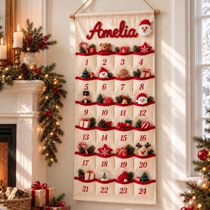 Könnte beinhalten: Ein cremefarbener Adventskalender aus Stoff zum Aufhängen mit dem Namen Amelia in roter Schrift oben. Er hat vierundzwanzig nummerierte Taschen mit rotem Rand, die jeweils kleine festliche Ornamente wie einen Teddybären, einen Weihnachtsmann und Geschenke enthalten.