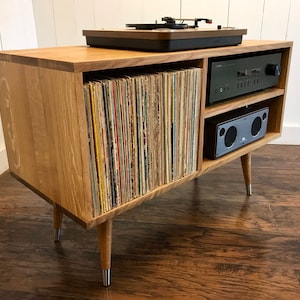 May include: A wooden record player stand with a turntable, amplifier, and speakers. The stand has a shelf for storing records and a lower shelf for a receiver. The stand has four legs.