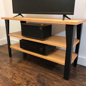 May include: A wooden entertainment center with black metal legs and two shelves. A black speaker and a black receiver are on the shelves.