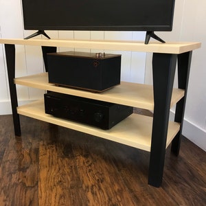 May include: A wooden entertainment center with black metal legs. The center has two shelves and is holding a television, a speaker, and an amplifier.