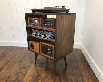 May include: A walnut wood stereo cabinet with a record player, speakers, and a shelf for books and media. The cabinet has a mid-century modern design with tapered legs.