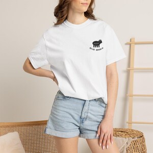 May include: A white short-sleeve t-shirt featuring a small black graphic of a stylized bear on the left chest area. Below the bear graphic, the text BEAR MINIMUM is printed in black capital letters. The shirt has a crew neckline and a relaxed fit.