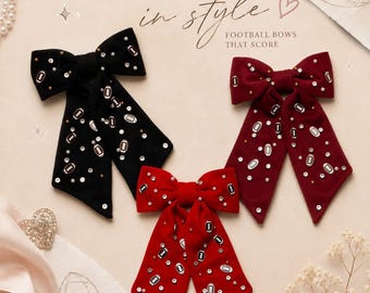 May include: Three fabric hair bows in black, maroon, and red, each featuring scattered silver-toned football charms and small white faux pearls. The text "TOUCHDOWN in style FOOTBALL BOWS THAT SCORE" is printed in black above the hair accessories.
