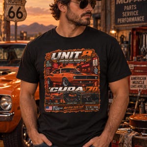 May include: A black t-shirt featuring a graphic print of an orange 1970 Plymouth Cuda. The design includes the text 'UNIT 8', 'AMERICAN MUSCLE', 'CUDA 70', and 'MAKE EVERY DRIVE COUNT', along with smaller images of the car's engine and interior details.