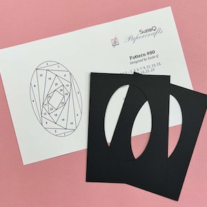 May include: A craft pattern and two black paper mats with oval cutouts. The pattern, labeled "Pattern #80," features a geometric design with numbered sections. The mats are positioned to the right, with a pink background.