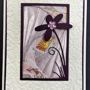 May include: A handmade greeting card with a floral design. The card features a cream-colored background with an embossed pattern. A dark purple flower with a pink gem center is the focal point, set against a geometric background.