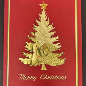 May include: A handmade Christmas card with a red background and a gold-colored Christmas tree design. The tree is topped with a gold star and the words "Merry Christmas" are written in gold script. The card has a gold and green border.