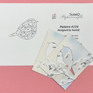 May include: A papercraft pattern with a bird design. The pattern includes a diagram with numbered sections and the text "Pattern #134 Designed by SuzieQ." Several cut-out bird shapes with a winter scene are also present, with snowy branches and a blue sky.