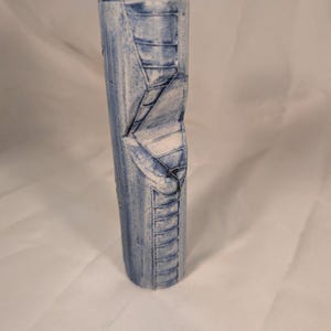 May include: A tall, cylindrical ceramic vase featuring a white base with a distressed blue wash finish. The exterior surface is decorated with a carved, recessed design depicting a winding staircase that spirals vertically along the side of the vessel.