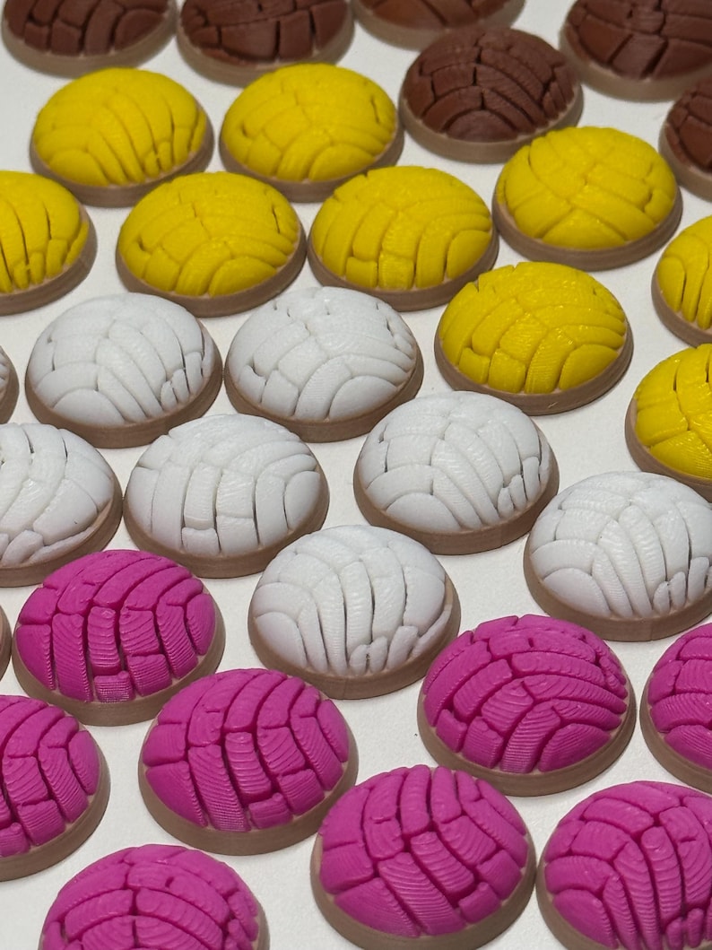 Puede incluir: Una colecci&oacute;n de miniaturas de pan concha, peque&ntilde;as, redondas y en forma de c&uacute;pula, en colores amarillo brillante, blanco y rosa vibrante. Cada pieza presenta un patr&oacute;n texturizado en forma de concha en la parte superior, imitando el pan dulce.