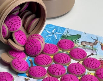 Puede incluir: Un recipiente cilíndrico de color canela volcado de lado, derramando numerosas fichas pequeñas, redondas y de color rosa brillante con forma de concha. Las fichas presentan un patrón de cuadrícula texturizado en la parte superior y están esparcidas sobre un tablero de juego ilustrado.