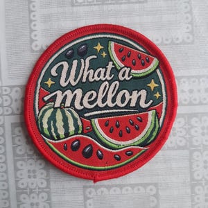 May include: A circular embroidered patch with a red border featuring a dark green background, illustrations of watermelon slices, and the text "What a mellon" in white script lettering, accented with small yellow stars and black seeds.