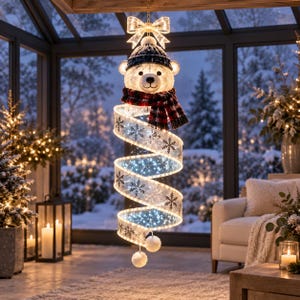 Può includere: Una decorazione luminosa sospesa con una testa di orso polare bianca che indossa un berretto in maglia blu scuro e una sciarpa a quadri rossi e neri. Sotto pende un lungo nastro a spirale traslucido con motivi a fiocchi di neve e LED bianchi.