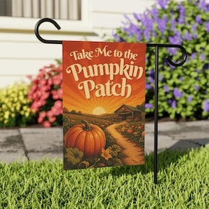 May include: A rectangular garden flag hanging on a black metal stand, featuring an orange sunset over a pumpkin patch with a barn and the text Take Me to the Pumpkin Patch in cream-colored lettering against a warm orange and red gradient sky.